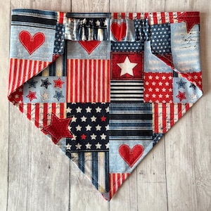 May include: Patriotic dog bandana with a patchwork design featuring red hearts, white stars, and red and white stripes on a blue background. The bandana is made of fabric and has a triangular shape.