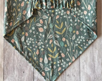 May include: A teal dog bandana with a floral pattern featuring peach, yellow, and white botanical elements. The bandana has a ruffled top edge and a triangular shape, designed to be tied around a pet's neck.
