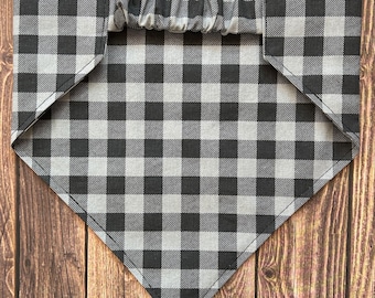 May include: A black and white checkered bandana with a gray elastic band. The bandana is folded into a triangle shape and is lying flat on a wooden surface.