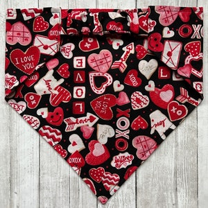 May include: Black bandana with a red and white Valentine's Day print featuring hearts, arrows, and the words "I Love You", "XOXO", and "Love".