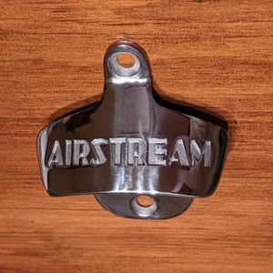 May include: A silver bottle opener with the word "AIRSTREAM" engraved on the front.