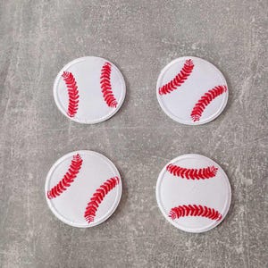 Könnte beinhalten: Vier weiße Baseball-Patches mit roter Naht. Jeder runde Patch zeigt das ikonische rote Nahtmuster eines Baseballs. Die Patches sind auf einer grauen Oberfläche angeordnet.