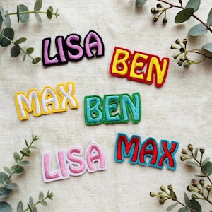 Könnte beinhalten: Sechs bestickte Stoffaufnäher mit den Namen LISA, BEN und MAX in verschiedenen Farben wie Pink, Gelb, Rot und Blau. Jeder Aufnäher hat einen dicken gestickten Rand und eine kräftige Schrift, angeordnet in einer verstreuten Anordnung.