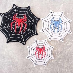 Könnte beinhalten: Drei gestickte Aufnäher mit Spinnennetzen und Spinnen. Ein Aufnäher ist schwarz mit einer roten Spinne, ein anderer ist weiß mit einer blauen Spinne, und der dritte ist weiß mit einer roten Spinne. Geeignet für Kleidung oder Accessoires.