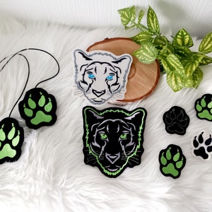 Könnte beinhalten: Ein Set Bügelbilder mit schwarzen und weißen Panther- und weißen Tigergesichtern mit grünen Pfotenabdrücken.