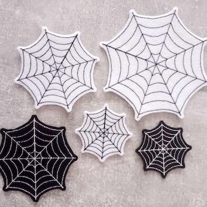 Könnte beinhalten: Fünf schwarze und weiße Filz-Spinnennetz-Patches. Die Patches sind in verschiedenen Größen und perfekt, um jedem Bastelprojekt eine gruselige Note zu verleihen.