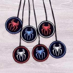 Könnte beinhalten: Sechs runde, schwarze und weiße gestickte Patches mit einem Spinnennetz-Design. Die Patches sind rot, blau und weiß. Die Patches sind an schwarzen Schnüren befestigt.