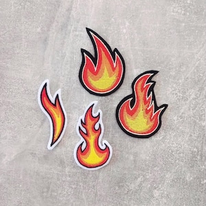 Könnte beinhalten: Vier gestickte Aufnäher in Flammenform in verschiedenen Größen und Designs. Jeder Aufnäher zeigt einen Farbverlauf aus gelbem, orangem und rotem Garn mit einem markanten schwarzen Rand. Die Formen umfassen eine hohe Flamme, eine breite und zwei kleinere.