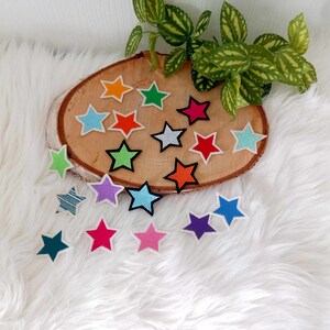 Könnte beinhalten: Eine Sammlung bunter Filzsternformen auf einer Holzscheibe. Die Sterne sind in verschiedenen Farben, darunter Blau, Grün, Rot, Pink und Gelb.