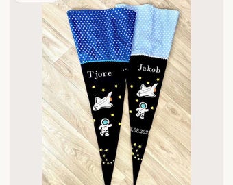 Può includere: Due sacchetti regalo in tessuto a forma di cono con una sezione inferiore nera decorata con grafiche di navette spaziali, astronauti e stelle gialle, con i nomi Tjore e Jakob. Le parti superiori sono blu e azzurre con pois bianchi.
