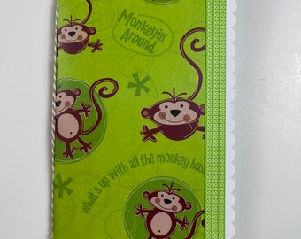 Puede incluir: Papel de regalo verde con un patrón de mono. Los monos son marrones con caras blancas y sostienen plátanos. El papel tiene el texto "Monkeyin' Around" y "What's up with all the monkey business?" impreso en él.