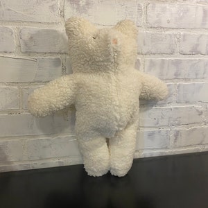 May include: A white plush teddy bear with a soft, fluffy texture. The bear is standing upright with its arms outstretched.