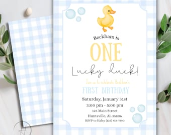 Puede incluir: Una invitación para baby shower con una ilustración de pato amarillo y el texto "Beckham is ONE Lucky duck!". La invitación tiene un borde con estampado de cuadros vichy azul claro y un sobre a juego. La invitación incluye la fecha, hora y lugar del evento.