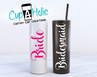 May include: Two insulated tumblers, one white with "Bride" in pink script, the other black with "Bridesmaid" in white script. Both have black straws. The logo "Cup A Holic" is at the top.