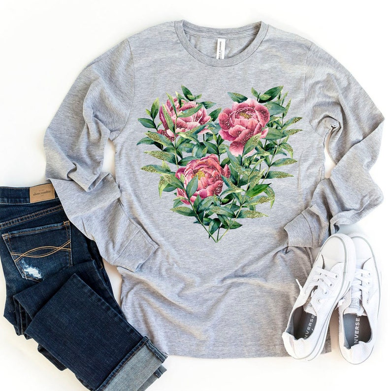 May include: A gray long-sleeved t-shirt with a floral design in the shape of a heart. The flowers are pink and green with gold glitter accents.