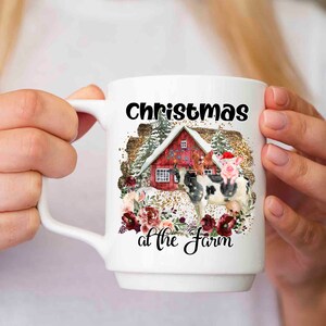 Puede incluir: Taza de cer&aacute;mica blanca con un dise&ntilde;o de Navidad en la granja. El dise&ntilde;o presenta un granero rojo con luces, una vaca, un cerdo con un gorro de Pap&aacute; Noel y una escena de invierno nevada.