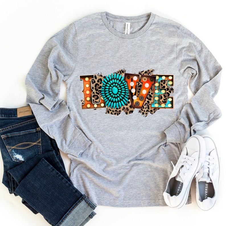 May include: A gray long-sleeve shirt with a graphic of the word "LOVE" in colorful, vintage-style letters with turquoise and brown accents. The letters are set against a leopard print background.