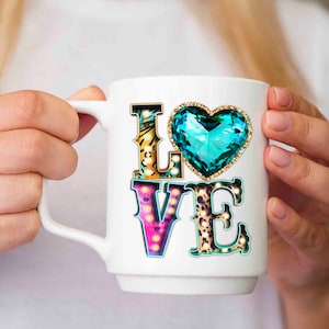 Puede incluir: Taza de cer&aacute;mica blanca con un dise&ntilde;o de "LOVE" colorido. Las letras est&aacute;n decoradas con patrones de estampado animal y bombillas. Un gran coraz&oacute;n de gema turquesa se encuentra sobre las letras.