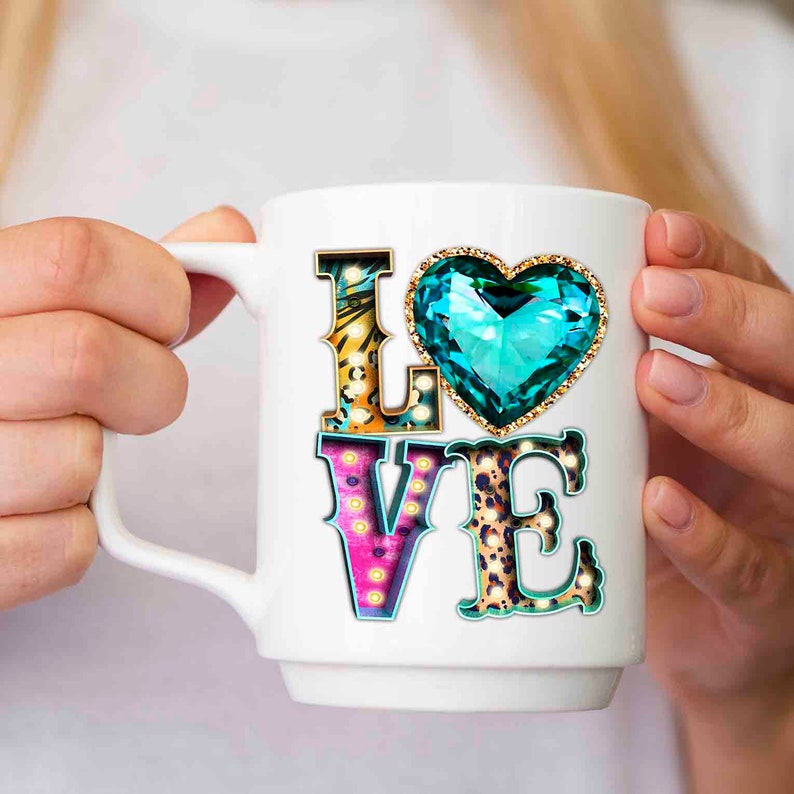 Puede incluir: Taza de cer&aacute;mica blanca con un dise&ntilde;o de "LOVE" colorido. Las letras est&aacute;n decoradas con patrones de estampado animal y bombillas. Un gran coraz&oacute;n de gema turquesa se encuentra sobre las letras.
