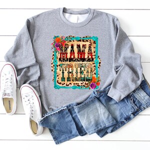 Puede incluir: Sudadera gris con un estampado gr&aacute;fico de un fondo de estampado de leopardo con ribete de cuerda turquesa y el texto "Mama Tried" en rojo, blanco y azul. El gr&aacute;fico est&aacute; rodeado de flores.