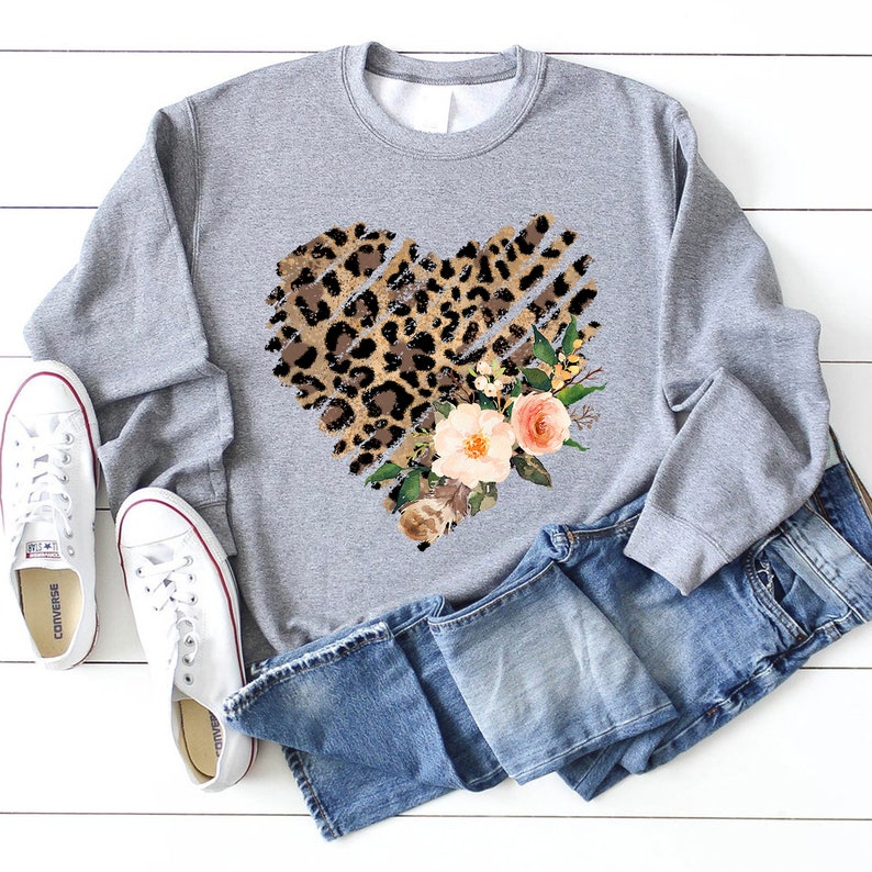 May include: A gray sweatshirt with a heart-shaped design featuring a leopard print and floral accents. The heart is outlined with a distressed, ripped effect.