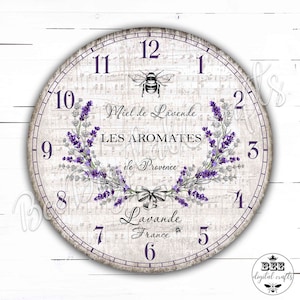 Puede incluir: Una esfera de reloj blanca con marcadores de hora en números romanos negros y marcadores de minutos en números arábigos negros. La esfera del reloj tiene un diseño floral de lavanda con una abeja y el texto "Miel de Lavende LES AROMATES de Provence Lavande France".