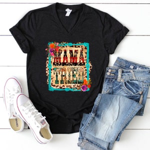 Puede incluir: Camiseta negra de cuello en V con un gr&aacute;fico de un marco de cuerda turquesa con fondo de estampado de leopardo. El texto "Mama Tried" est&aacute; en rojo, blanco y azul con detalles florales.