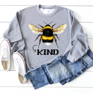 May include: Gray sweatshirt with a black and yellow bumblebee graphic and the word "KIND" in black text.