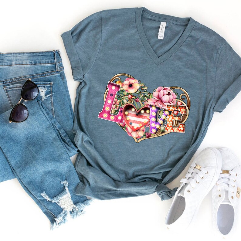 Puede incluir: Una camiseta de cuello en V azul turquesa con un gr&aacute;fico de la palabra "LOVE" en forma de coraz&oacute;n. Las letras est&aacute;n decoradas con luces y flores.