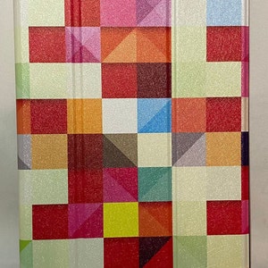 May include: A rectangular tablet case with a colourful geometric pattern. The design features squares and triangles in shades of red, orange, pink, yellow, green, blue, and white. The case has a textured, glittery finish.