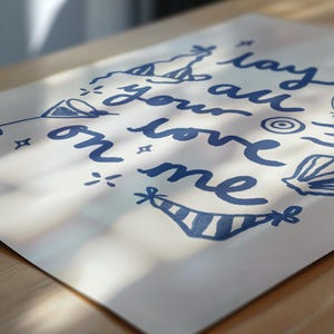 May include: A white card with blue ink lettering that says "lay your love on me" with various blue doodles around the text.