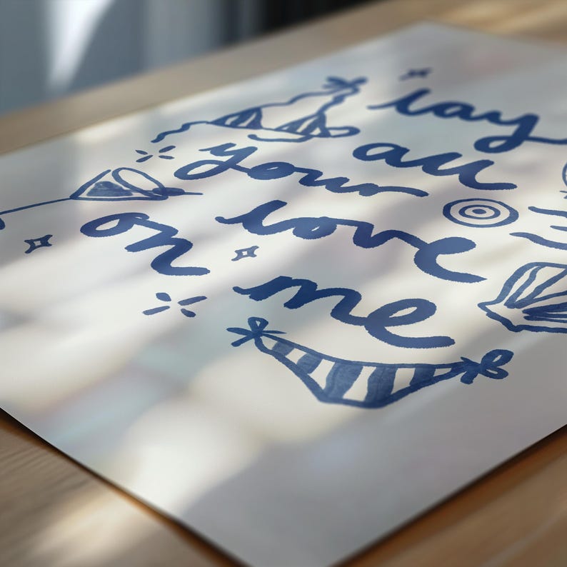 May include: A white card with blue ink lettering that says "lay your love on me" with various blue doodles around the text.