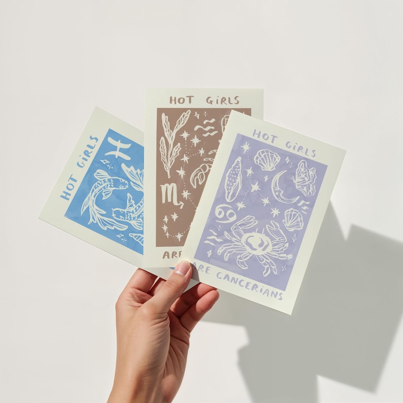 Puede incluir: Tres tarjetas con el texto "Hot Girls Are" seguido de un signo del zod&iacute;aco. La primera tarjeta es azul con Piscis, la segunda es marr&oacute;n con Escorpio y la tercera es morada con C&aacute;ncer.