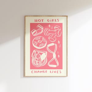 Può includere: Una stampa incorniciata con sfondo rosa e illustrazioni bianche di attrezzature per il fitness. Il testo "HOT GIRLS" è in alto e "CHANGE LIVES" in basso. La stampa include manubri, fasce di resistenza e un disco pesi.