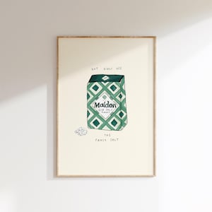 Op de afbeelding: Een ingelijste print met een aquarel illustratie van een Maldon zeezoutdoos. De doos heeft een groen en wit ruitpatroon. De tekst "HOT GIRLS USE" en "THE FANCY SALT" staan boven en onder de doos. Een kleine hoop zout staat naast de doos.