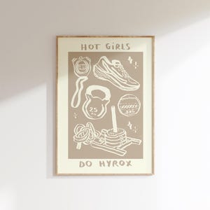 May include: A framed print with a beige background featuring white illustrations of fitness equipment, including a stopwatch, sneakers, kettlebell, and a medicine ball. The text "HOT GIRLS DO HYROX" is at the top and bottom.