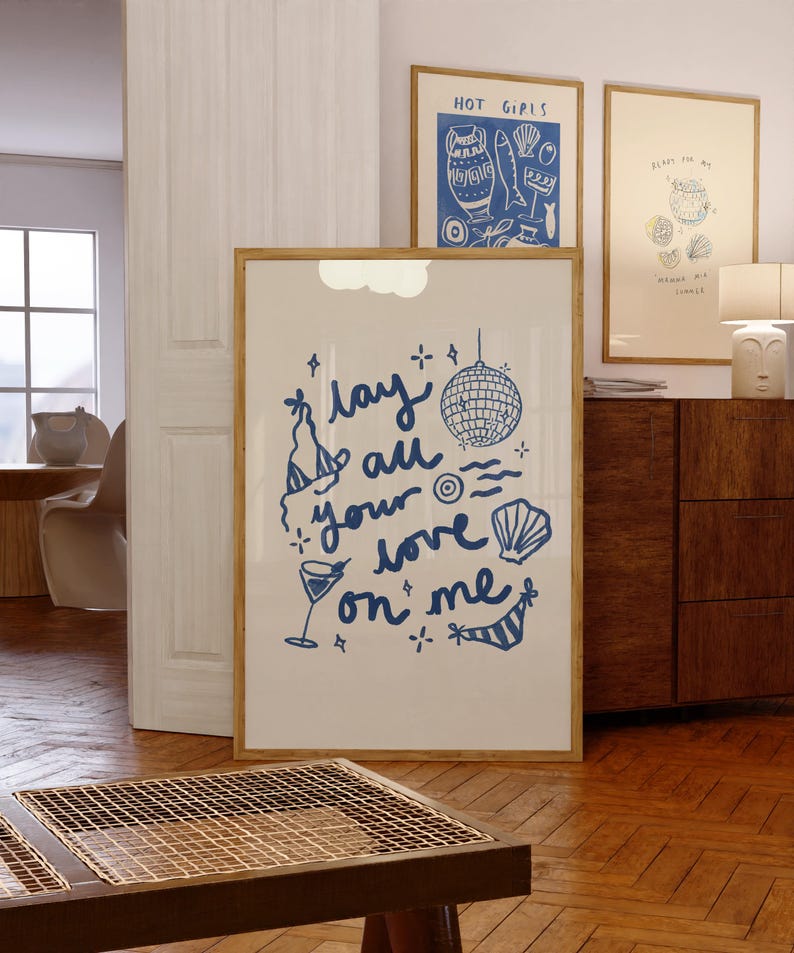 May include: A framed print with a blue and white illustration of a disco ball, a cocktail glass, and a seashell. The text "Lay all your love on me" is written in a whimsical font.