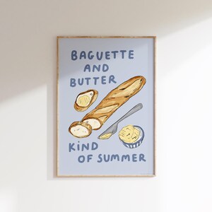 Könnte beinhalten: Ein gerahmter Druck mit einer Aquarellillustration eines Baguettes, Butter und eines Messers auf hellblauem Hintergrund. Der Text "Baguette and Butter Kind of Summer" ist in blauen Buchstaben dargestellt.