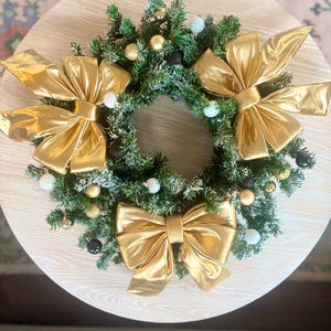 Ghirlanda sempreverde innevata, decorata con fiocchi dorati metallizzati e ornamenti bianchi, dorati e neri!