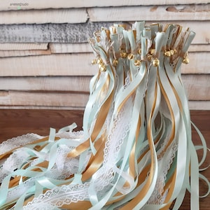 Könnte beinhalten: Ein Bündel aus hellblauem und goldenem Satinband mit weißer Spitzenborte und goldenen Glöckchen. Die Bänder sind oben zusammengebunden und hängen herunter.