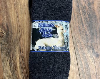 May include: Dark gray Ultimate Alpaca Socks, size L, with a label featuring an alpaca image and the words "Extreme Thermal." The socks are folded and displayed on a wooden surface.