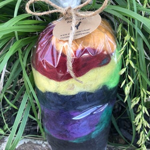 May include: A package of colorful alpaca fiber for felting. The fiber is layered in shades of red, yellow, black, purple, and green. The package is tied with twine and has a label that reads "Outlaw Farm Alpacas" and a website address.