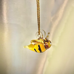Puede incluir: Un collar de cadena dorada con un colgante de abeja de vidrio. La abeja es amarilla y negra con alas transparentes.