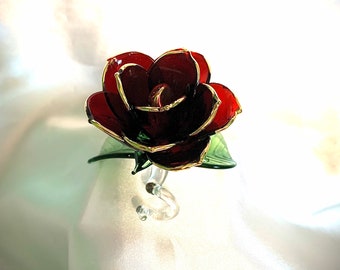 May include: A single red glass rose with gold trim and green leaves. The rose is on a clear glass stand.
