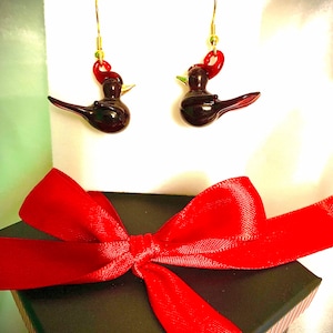 Könnte beinhalten: Ein Paar rote und schwarze Glasvogel-Ohrringe mit goldenen Haken. Die Ohrringe sind in einer schwarzen Geschenkbox mit roter Schleife verpackt.