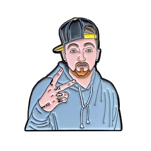 May include: A black and yellow baseball cap with a blue hoodie and a peace sign. The person in the image has a beard and a tattoo on their hand that says "XXX".