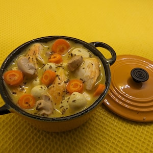 May include: A miniature yellow and black cast iron pot filled with a stew. The stew contains chicken, carrots, mushrooms, and small white onions. The lid is off to the side. The background is a solid yellow.