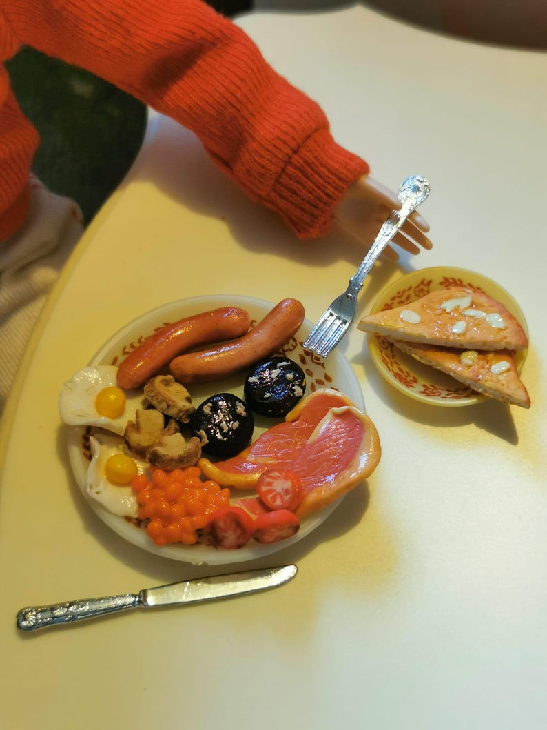 May include: Miniature full English breakfast on a white plate, including sausages, eggs, beans, mushrooms, tomatoes, and black pudding. A small plate of pizza slices is also present. A fork and knife are next to the plate. The scene is set on a light yellow surface.