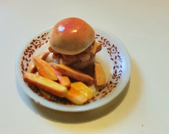 May include: A miniature ceramic burger with fries on a small plate. The burger has a glossy, reddish-brown bun and a stack of what appears to be a patty. The fries are a mix of yellow and orange. The plate has a white base with a brown floral pattern.