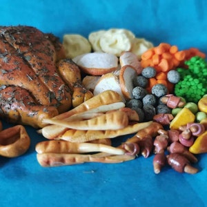 May include: A miniature Thanksgiving dinner arrangement on a blue surface. The arrangement includes a roasted turkey, Yorkshire puddings, parsnips, carrots, peas, and other side dishes. The turkey is seasoned with herbs.